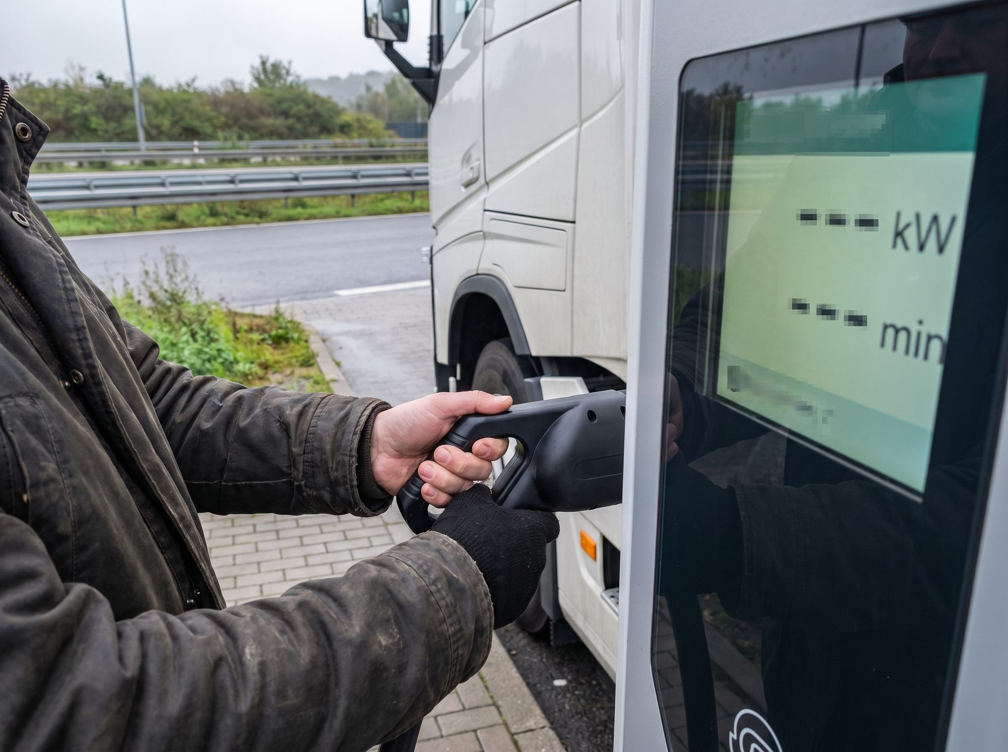 Fahrer prüft den Stecker an der Ladesäule, Servicenummer im Display